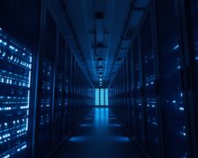 Interior of a data center with blue-lit server racks representing AI compute infrastructure.