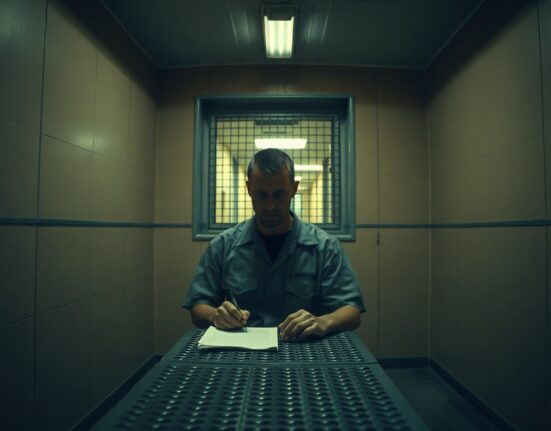 Sam Bankman-Fried in prison uniform sitting at a table with a notepad, planning a new cryptocurrency