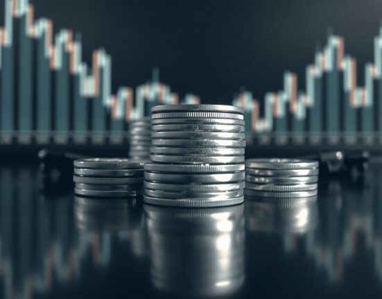 Silver bullion coins and bars on a reflective surface with a blurred financial chart in background