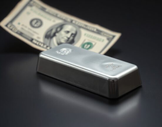 Silver bar on reflective surface with blurred dollar bill in background