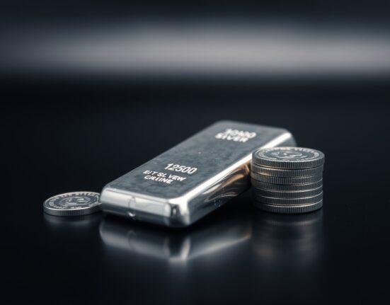 Silver bars and coins on a dark reflective surface with soft lighting