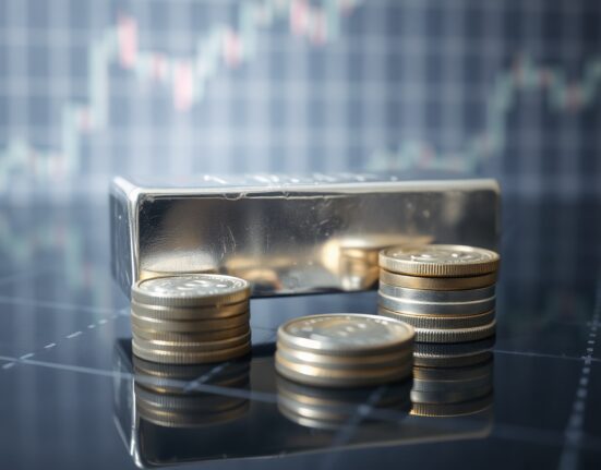 Silver bars and coins on a reflective surface with a soft financial chart pattern background, representing silver price analysis.