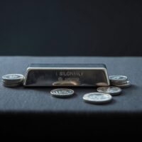Silver bars and coins reflecting light on a dark surface, representing precious metals market analysis.