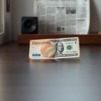 Singapore dollar and US dollar banknotes on a desk representing currency consolidation.