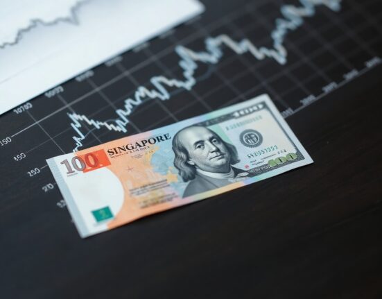 Singapore dollar and US dollar banknotes on a desk with financial chart background