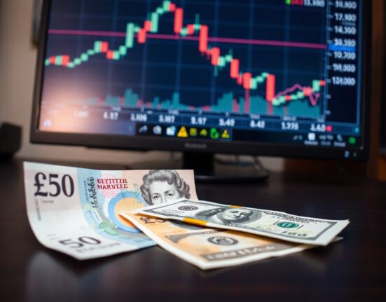 British Pound and US Dollar banknotes on a desk with a financial chart in the background