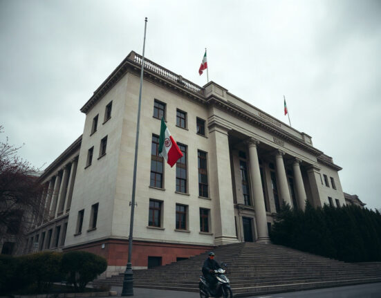 Iranian flag flying in front of a government building in Tehran under overcast skies.