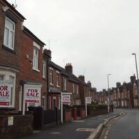 Residential street in the UK with multiple For Sale signs under overcast sky, reflecting housing market slowdown.