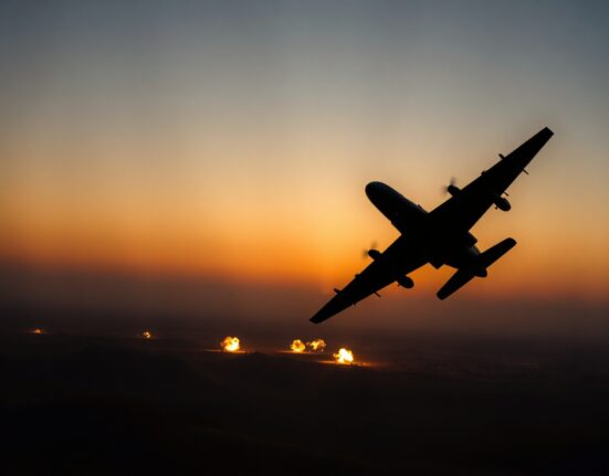 Military aircraft flying over desert with explosions on horizon during U.S. airstrikes on Iran