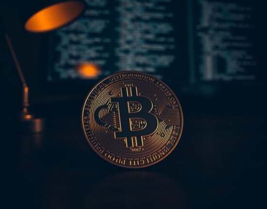 Bitcoin coin with U.S. Constitution text inscription on a desk with a computer monitor in background