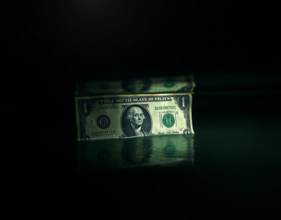 Weathered US dollar bill partially submerged in water, symbolizing questions about its reserve currency status.