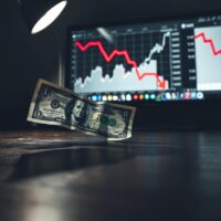 Crumpled US dollar bill on desk with bearish financial charts in background