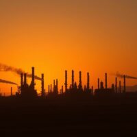 Oil refinery at dusk with smoke in distance after US strikes in Iran