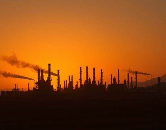 Oil refinery at dusk with smoke in distance after US strikes in Iran