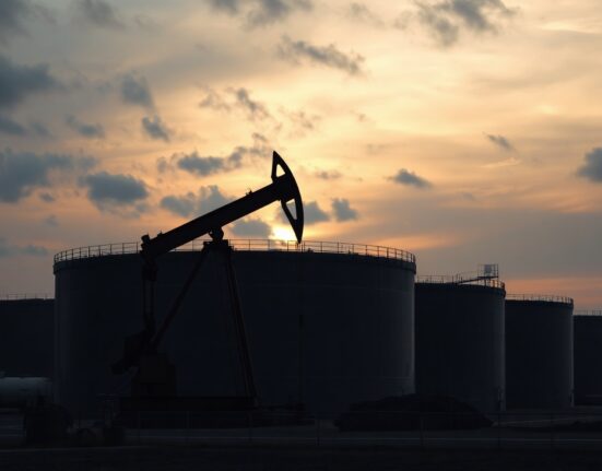 Oil pumpjack and storage tanks under overcast sky representing WTI price decline below $70