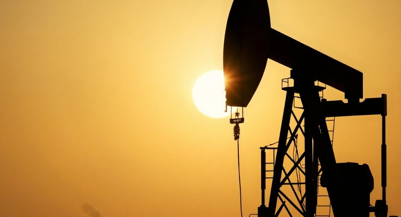 Oil pumpjack silhouetted at sunset with distant smoke, representing geopolitical oil supply risk