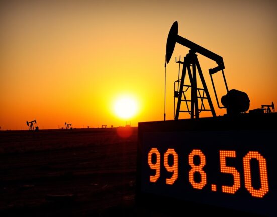 Oil pumpjack with digital price display showing WTI crude at $98.50 in a sunset oil field.