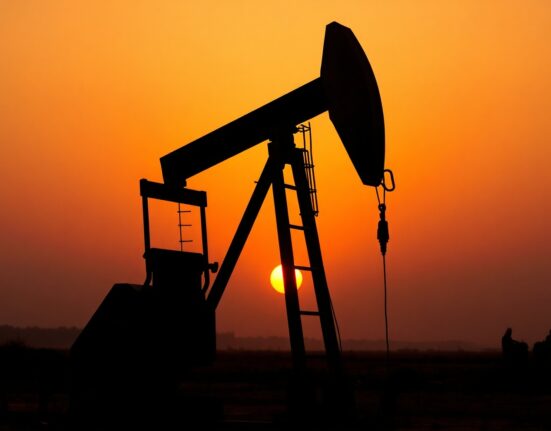 Oil pumpjack silhouette at sunset with smoky horizon representing Middle East tensions