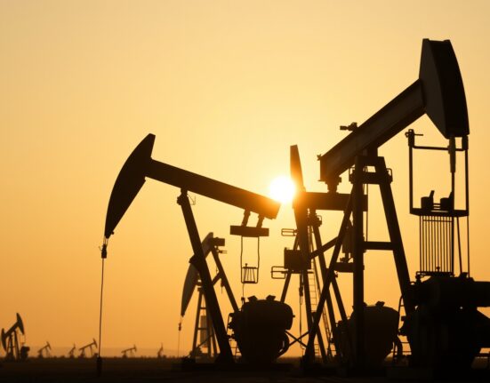 Oil pumpjacks silhouetted against a hazy sunset sky at a desert oil field, representing crude oil production.