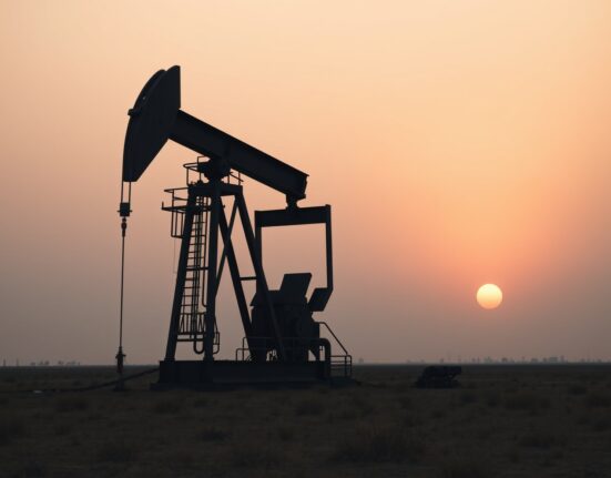 Silhouette of an oil pumpjack at sunset in a dry field, representing declining crude oil prices.