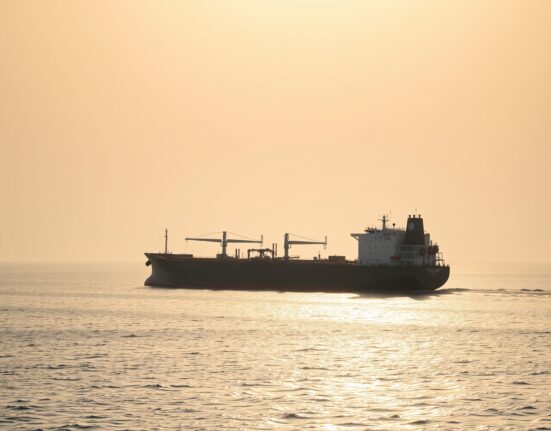 Aerial view of an oil tanker in the Strait of Hormuz, with calm waters and soft sunlight.