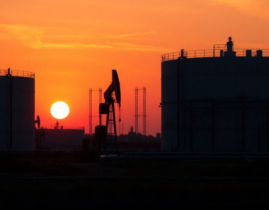 Oil storage tanks and pump jack at sunset, representing crude oil market and geopolitical risk