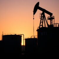 WTI crude oil storage tanks and pumpjack at an oil facility at sunset.