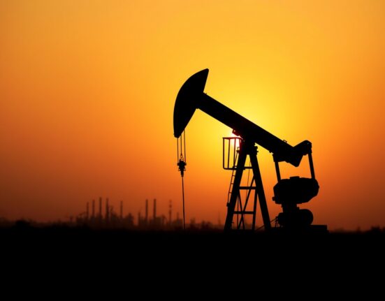 Oil pumpjack silhouetted at sunset with refinery in background representing crude oil supply dynamics