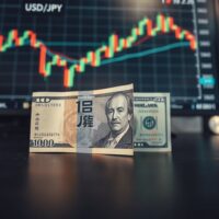 Japanese yen and US dollar banknotes on a trading desk with a monitor showing USD/JPY charts